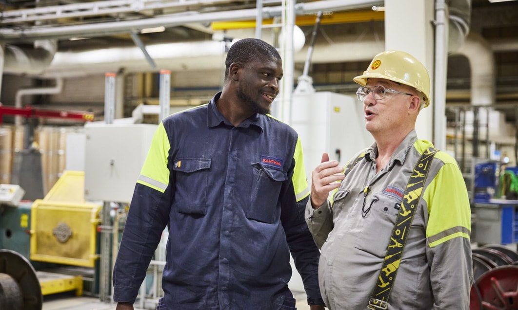 en person i skyddshjälm pratar med en person i en fabrik