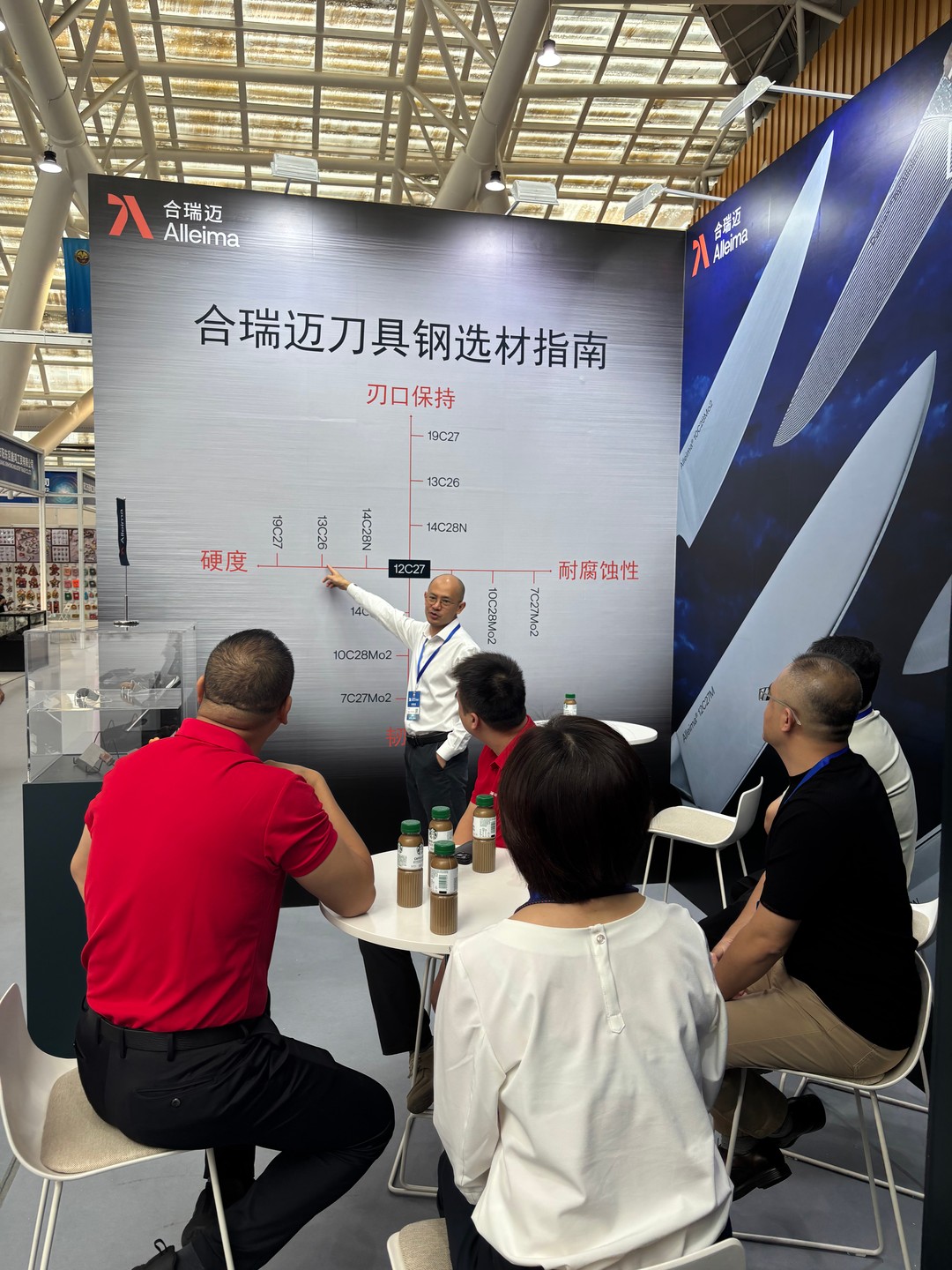 A man from Alleima displays Alleima's steel grades  on large poster with people sitting around it 